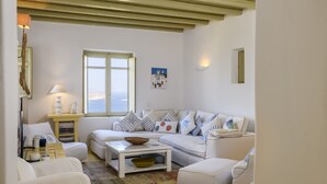 A white-themed living room with a sofa, a coffee table, and a window with a view. - Beautiful Villa Isabella (Mykonos)