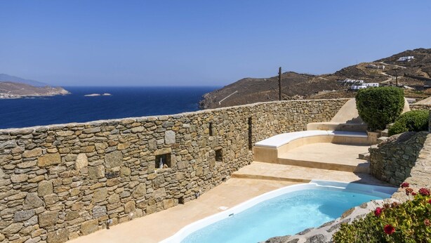 A stone-walled pool area with a clear view of the sea and a hilly landscape in the background. - Beautiful Villa Isabella (Mykonos)