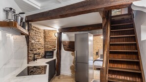 Una cocina con pared de piedra, vigas de madera, refrigerador de acero inoxidable y una escalera de madera.