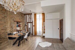 A dining area with a wooden table, chairs, and a chandelier. There is a stone wall and a wooden door in the background.