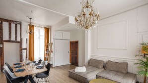 Un comedor con una mesa de madera preparada para cuatro personas, un sofá, una araña y una planta.