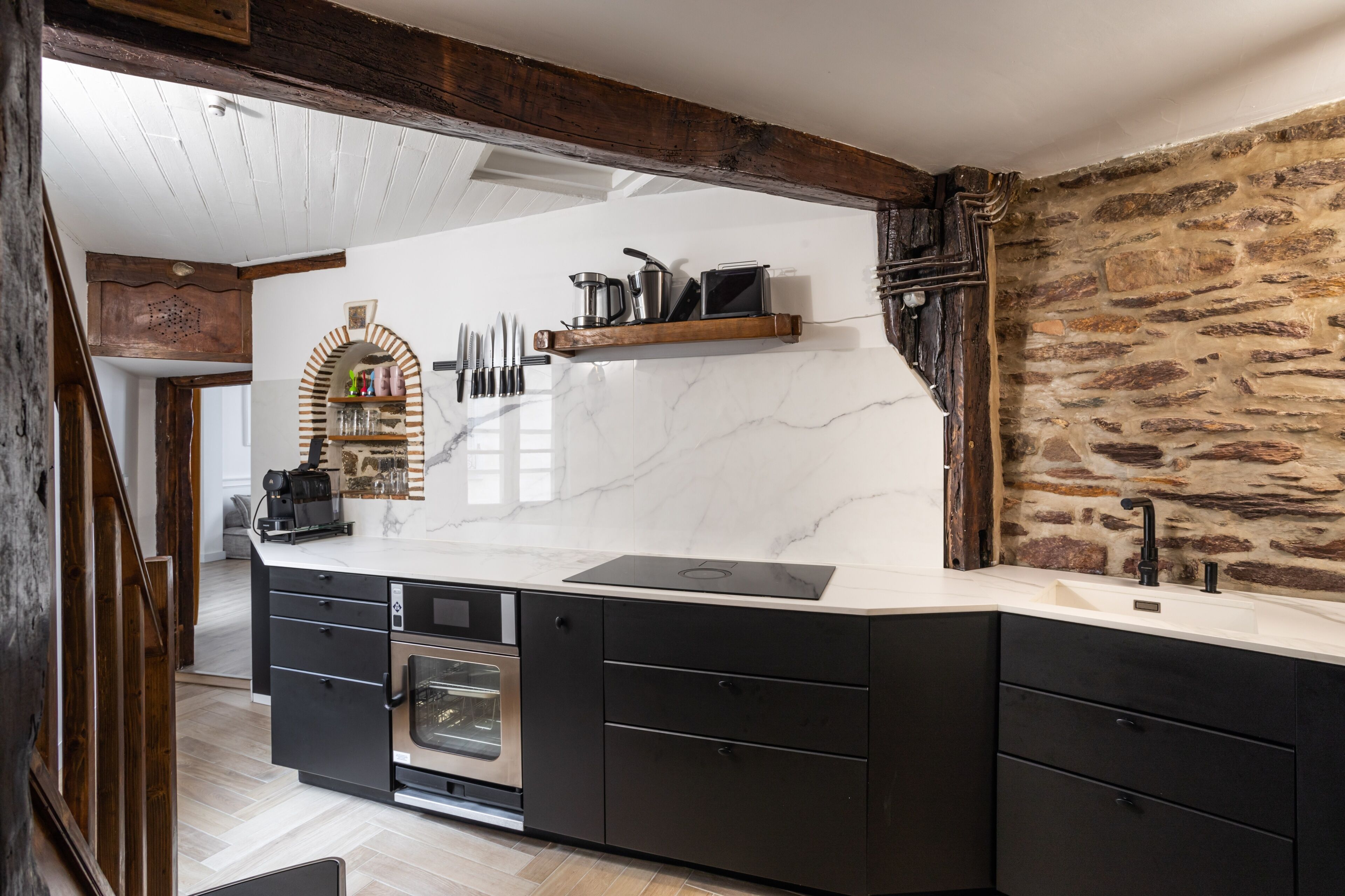 A modern kitchen with a marble countertop, built-in oven, and a stone wall.