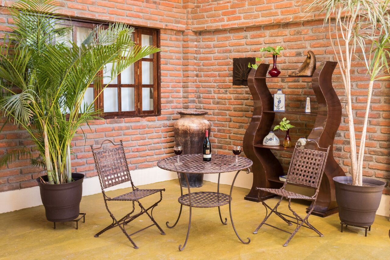 A cozy patio with a brick wall, a round metal table, two wicker chairs, and potted plants.