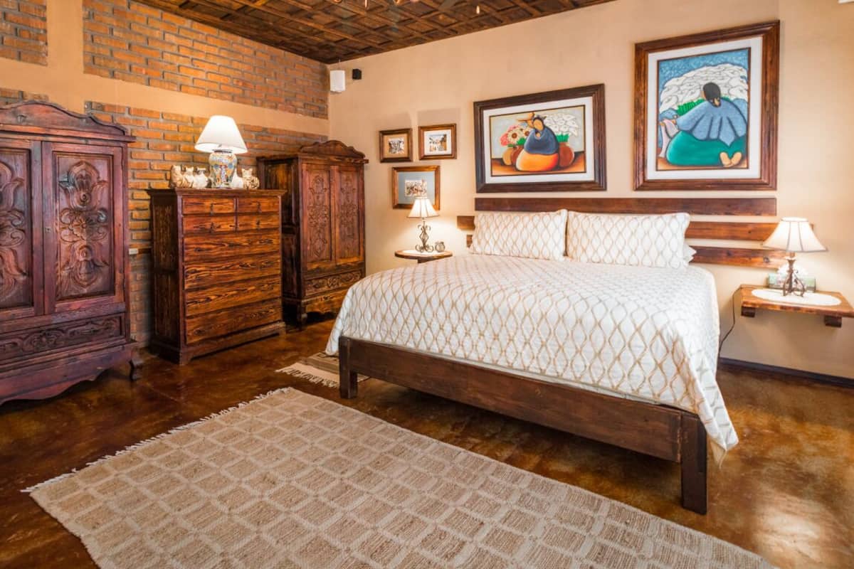 A bedroom with a wooden bed, a wooden dresser, and a brick wall.