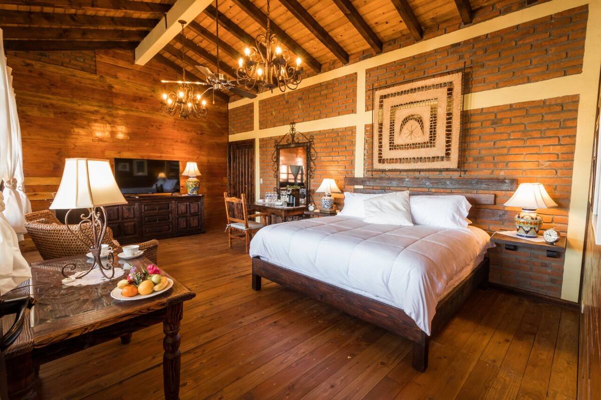 A cozy room with a large bed, wooden floors, a brick wall, a chandelier, and a television.