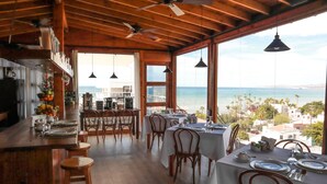 A dining area with tables set for four, wooden chairs, and a view of the ocean.
