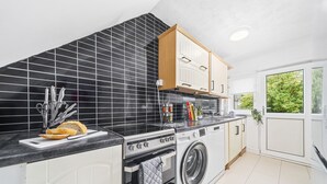 Une cuisine moderne avec un crédence en carreaux noirs, un four encastré, un lave-linge et un plan de travail équipé d’ustensiles de cuisine.