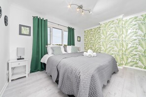 A bedroom with a bed, a nightstand, a window with curtains, and a wall with a leaf pattern.