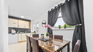 Une cuisine moderne avec des meubles blancs, un plan de travail en marbre et un coin repas comprenant une table en marbre et des chaises en cuir.