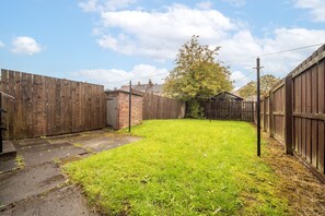 A fenced backyard with a grassy lawn, a brick structure, and a tree.