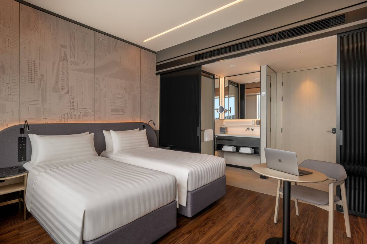 A modern hotel room with a large bed, a desk, a laptop, and a mirror.