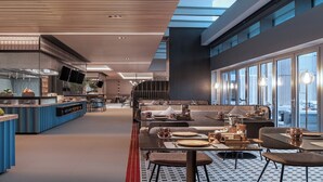 A modern restaurant with a long counter, seating area, and large windows.