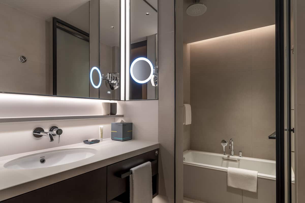 A modern bathroom with a large mirror, two sinks, a bathtub, and a glass shower enclosure.