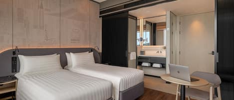 Una habitación de hotel moderna con una cama grande, un escritorio con una laptop y una pequeña zona de estar.