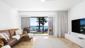A modern living room with a brown leather sofa, a white rug, and a large flat-screen TV. - Luxury Beachfront Retreat | Henley Beach Esplanade (Henley Beach)