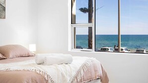 A bedroom with a large window overlooking the sea, a bed with pink bedding, and a white wall. - Luxury Beachfront Retreat | Henley Beach Esplanade (Henley Beach)