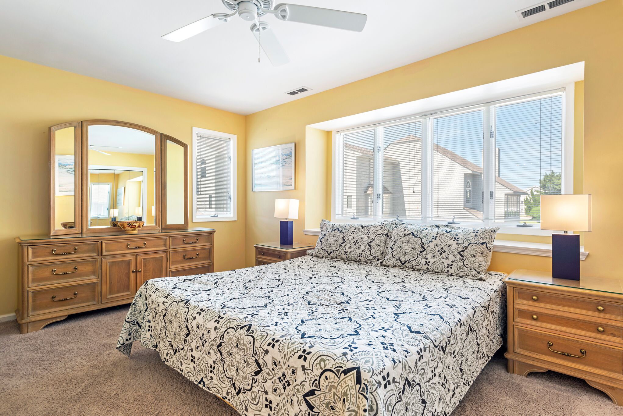 A bedroom with a large bed, a dresser, a mirror, and a window with blinds.