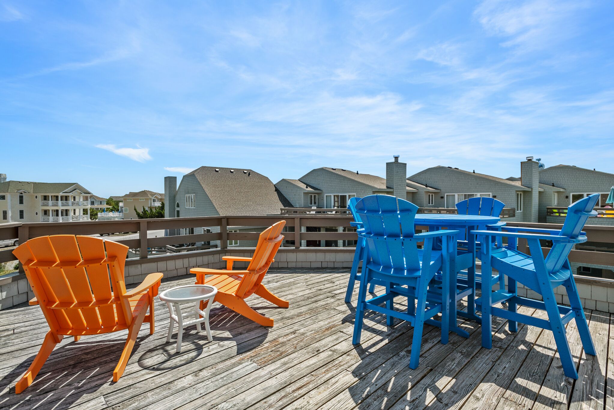 Een houten terras met tuinmeubilair, waaronder oranje en blauwe stoelen en een kleine tafel.