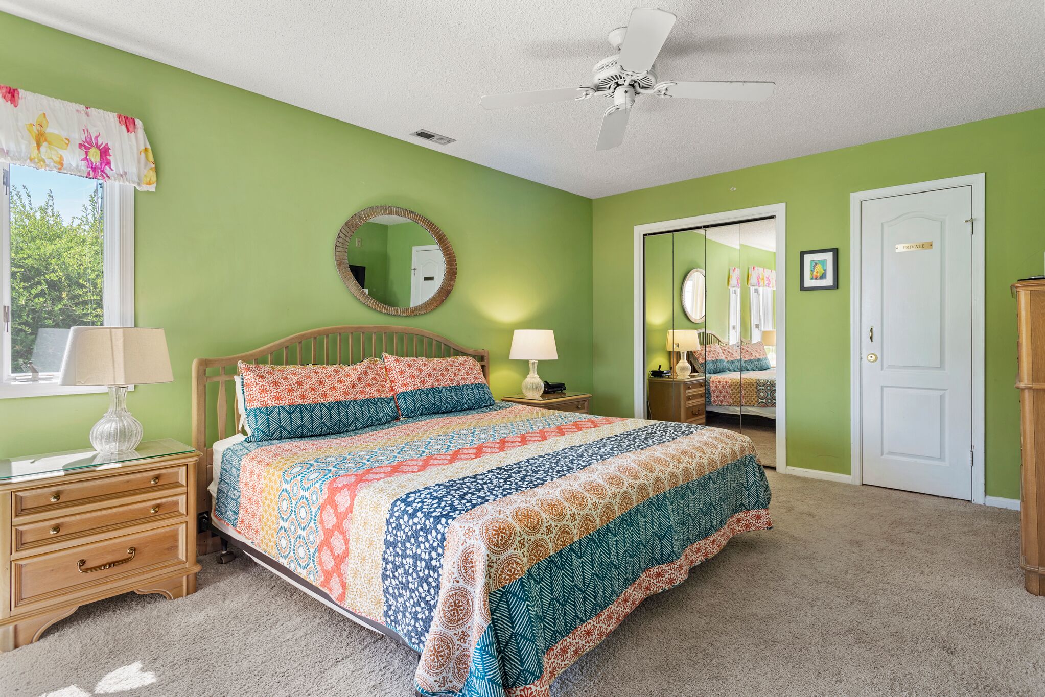 A bedroom with a bed, nightstands, a mirror, and a door.