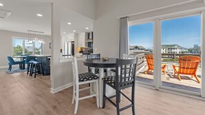 Eine moderne Küche mit weißen Schränken, ein Essbereich mit rundem Tisch und Stühlen sowie ein Balkon mit orangefarbenen Stühlen.