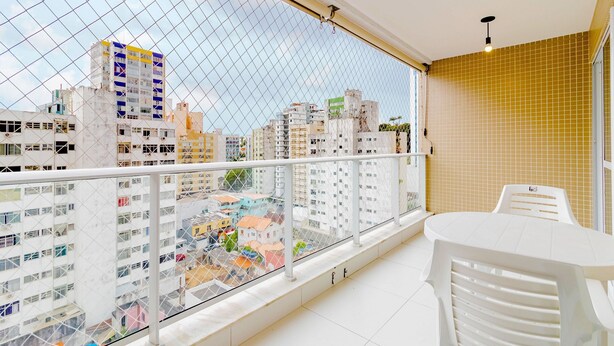 A balcony with a view of a cityscape, featuring a white table and chairs, and a yellow-tiled wall.