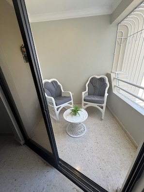 A balcony with two white wicker chairs, a small round table with a plant, and a metal railing.