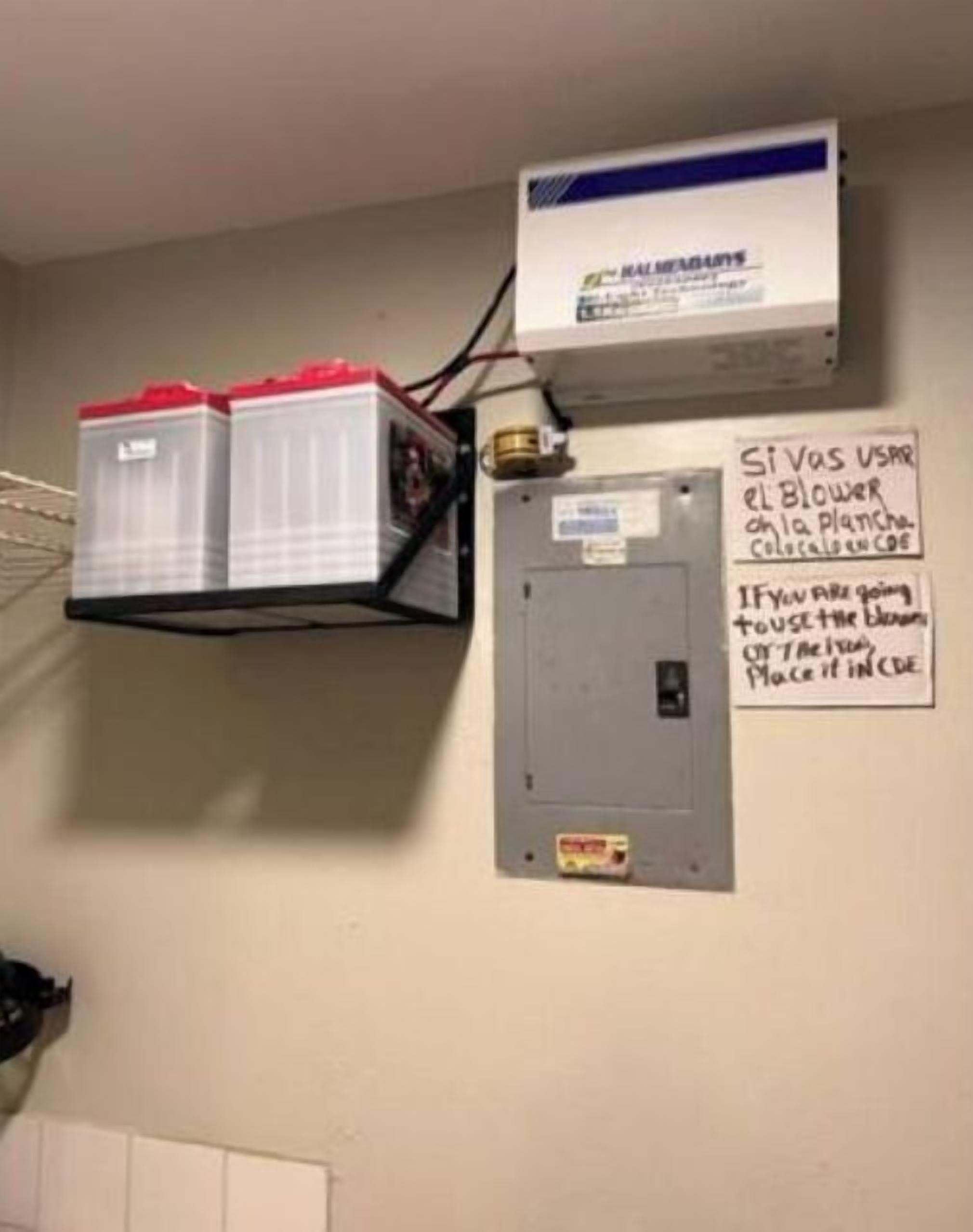 Une pièce utilitaire équipée d’un grand climatiseur, de deux bacs de rangement à couvercle rouge et d’une pancarte manuscrite accrochée au mur.