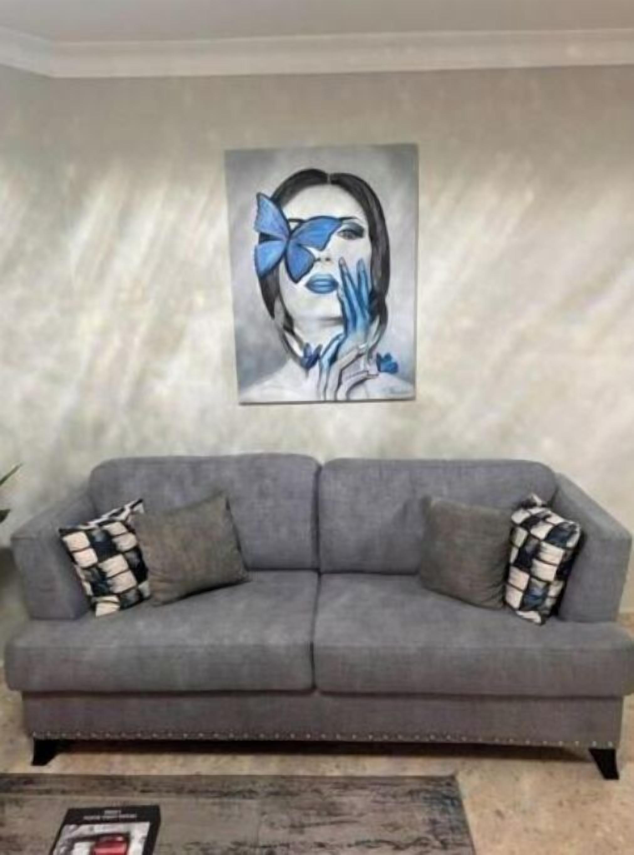 Un sofá gris con almohadones a cuadros, una obra de arte enmarcada en la pared y una pequeña alfombra en el suelo.