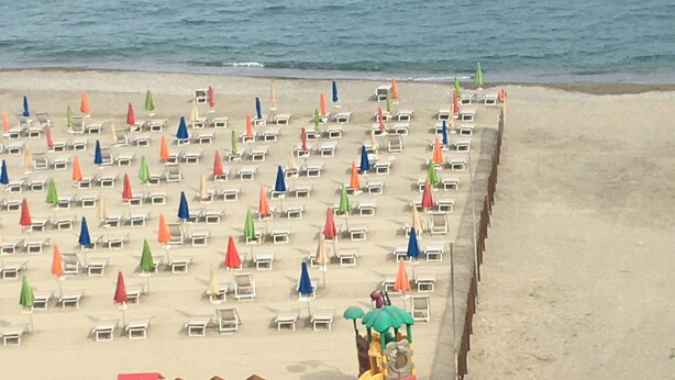 Una playa con filas de tumbonas y sombrillas, una zona de juegos para niños y vistas al mar.