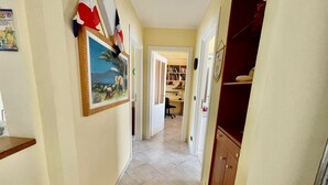 Un pasillo con piso de baldosas, un cuadro en la pared y una puerta que da a una habitación con un escritorio y una silla.