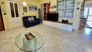 Una sala de estar con un sofá, televisión, mesa de vidrio y estanterías con banderas.