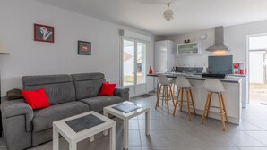 A modern living room with a grey sofa, a white coffee table, and a kitchen area with a bar stool. - Apartment with Private Terrace & Shared Garden (Mimizan)