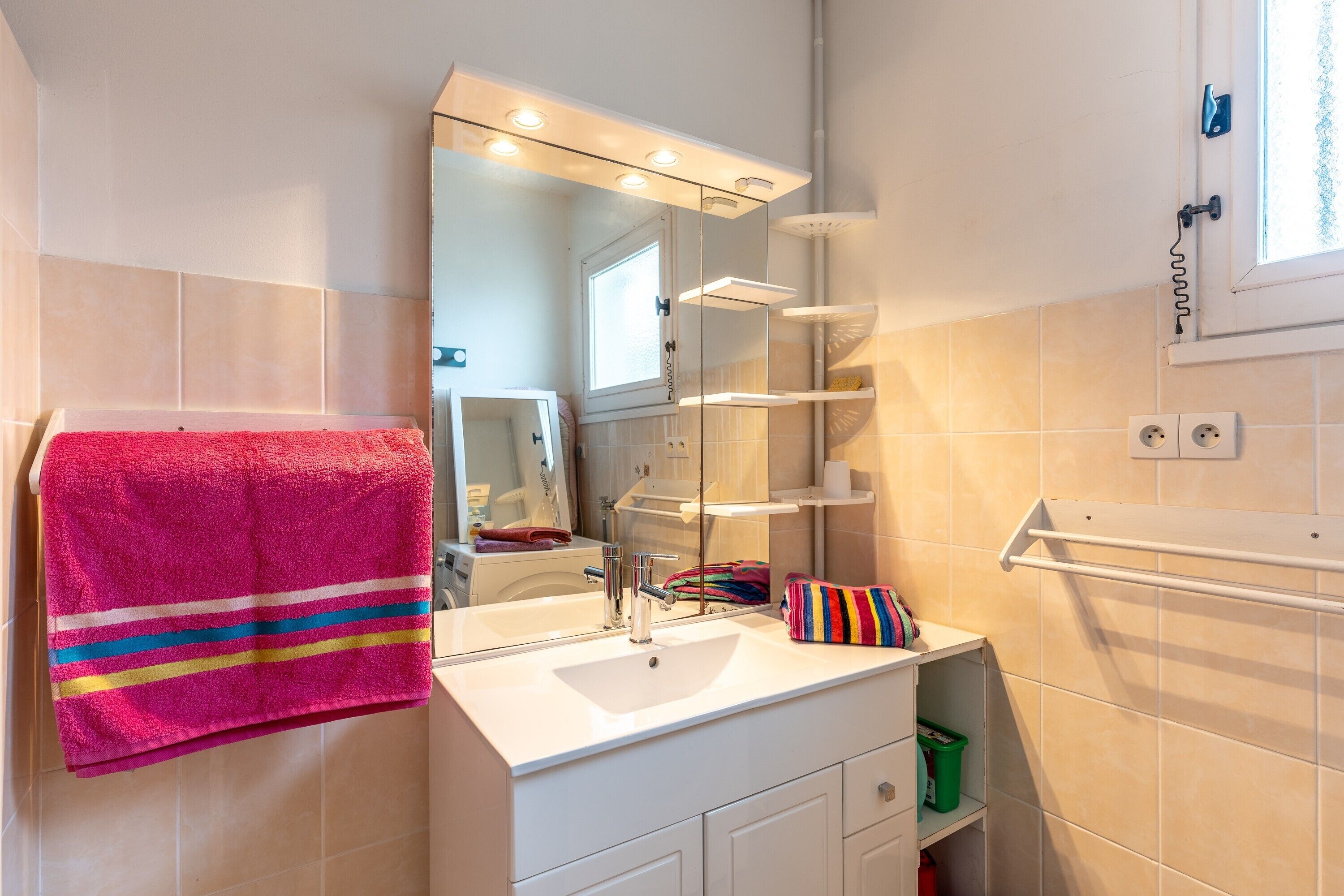 Un baño con lavamanos blanco, espejo y repisas.