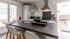 A modern kitchen with a central island, bar stools, a built-in oven, and a microwave. - Apartment with Private Terrace & Shared Garden (Mimizan)