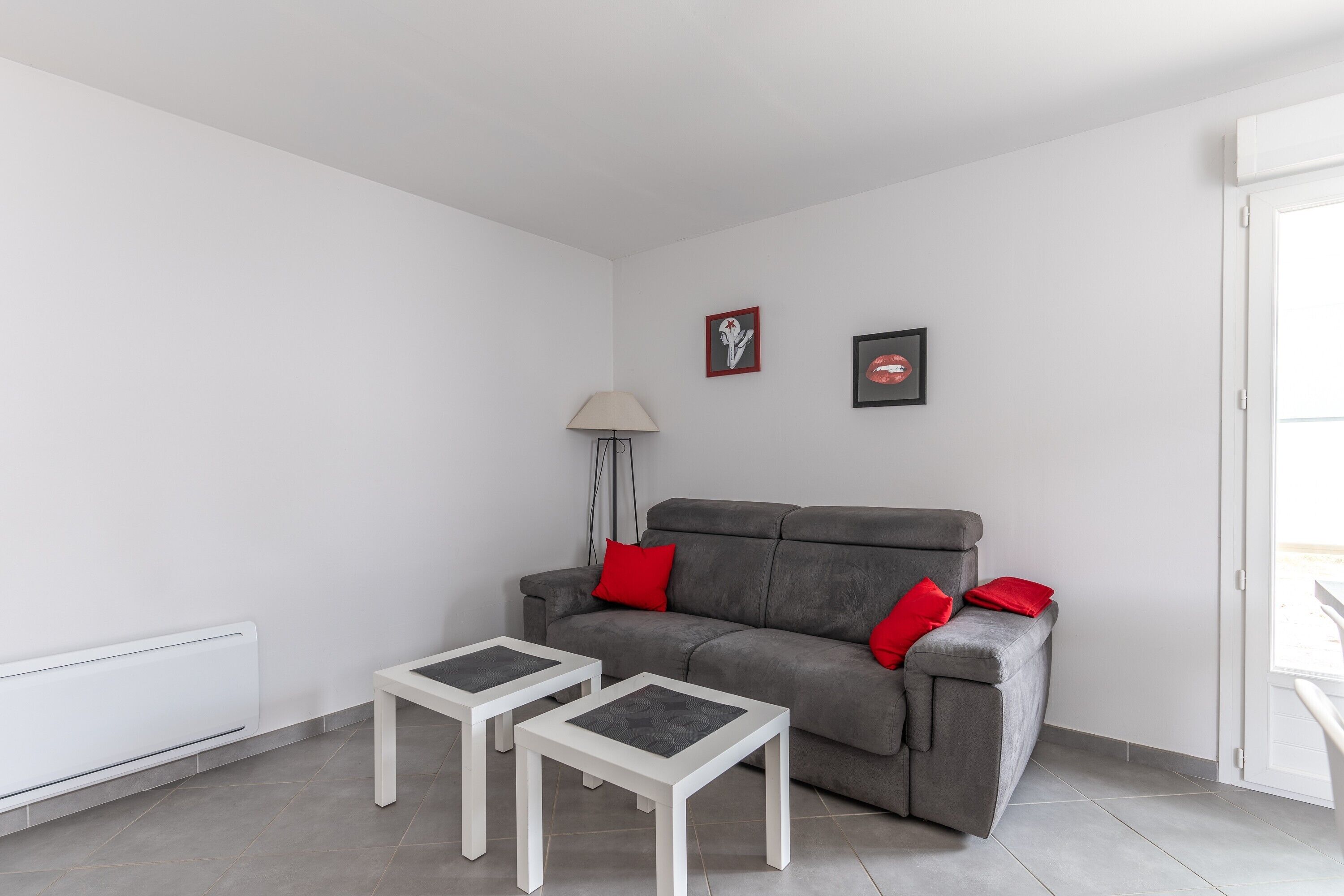 A modern living room with a grey sofa, two white side tables, a floor lamp, and two framed pictures on the wall.