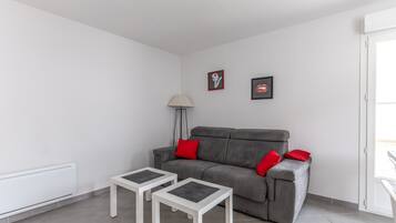 A modern living room with a grey sofa, two white side tables, a floor lamp, and two framed pictures on the wall.