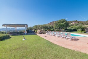 A poolside area with lounge chairs, a pergola, and a view of a mountainous landscape.