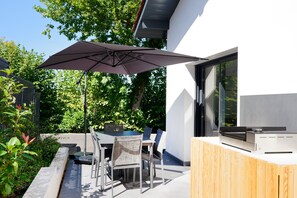 An outdoor patio with a table, chairs, and a large umbrella. - Vacation Home "Maison Aranea" with Mountain View, Private Terrace & Wi-Fi (Ascain)