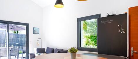 A modern room with a wooden table, grey sofa, and a blackboard with 'Bienvenue' written on it.