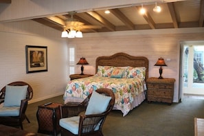 A bedroom with a large bed, two bedside tables, wicker chairs, and a framed picture on the wall.