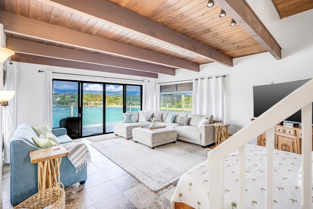 A spacious living room with a large window overlooking a scenic view, a wooden ceiling, and a modern sofa set.