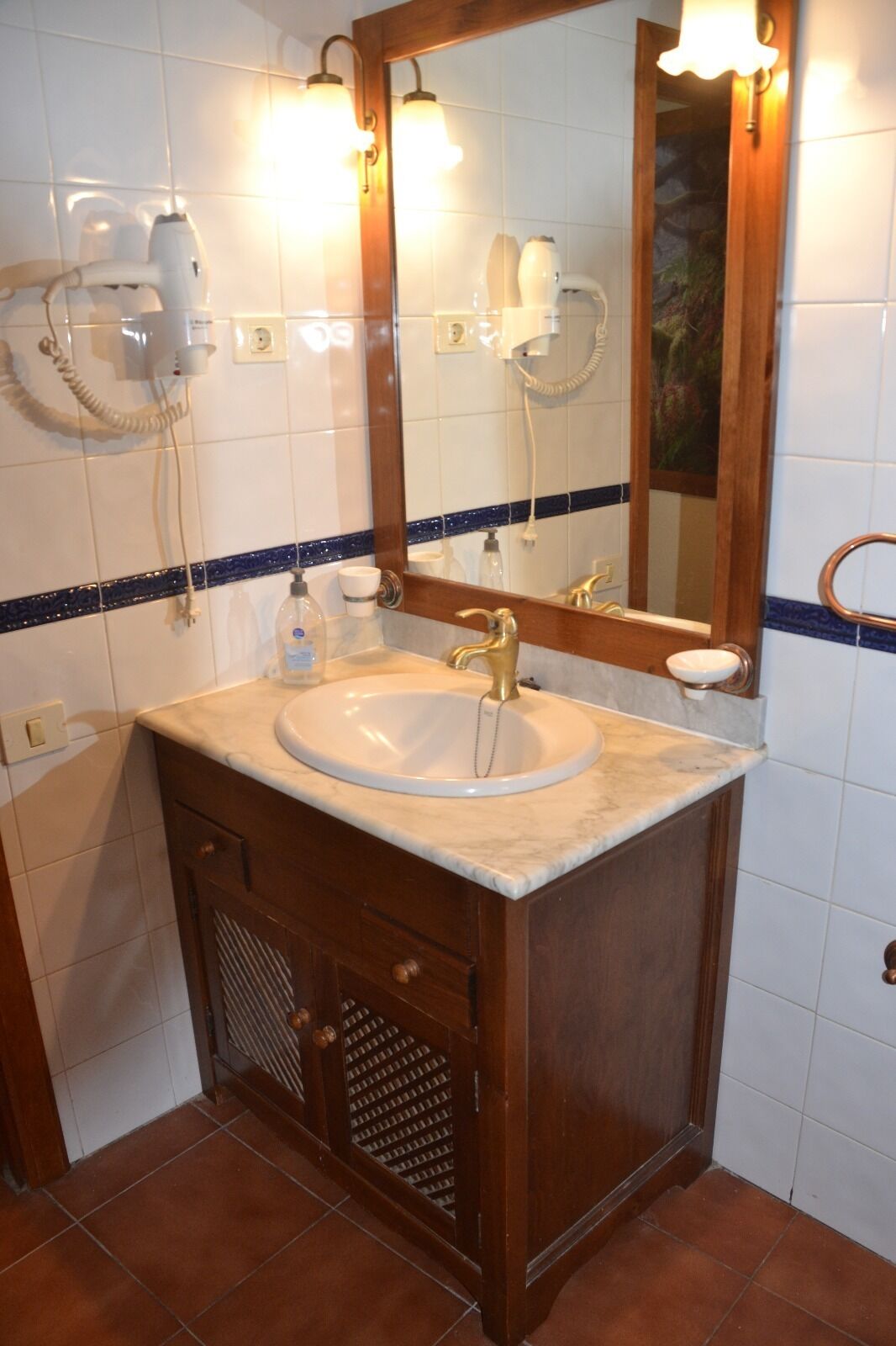 A bathroom with a white sink, wooden vanity, and a mirror with lights.
