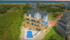 Une maison à plusieurs étages avec une piscine, entourée de verdure et offrant une vue sur la plage.