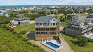Une grande maison à plusieurs étages, dotée d’une piscine et offrant une vue sur la plage.