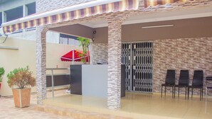 A covered outdoor seating area with a reception desk, a potted plant, and a red umbrella. - Residences Hydlyss (Abidjan)