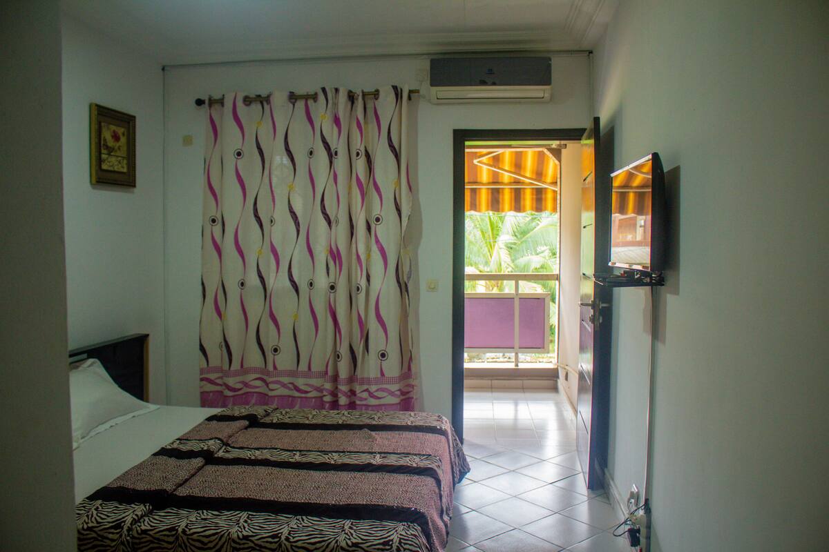 A bedroom with a bed, curtains, a television, and a door leading outside.