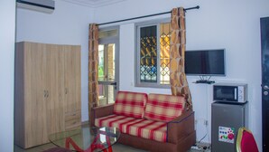 A living room with a sofa, a glass table, a television, a microwave, and a wardrobe. - Residences Hydlyss (Abidjan)