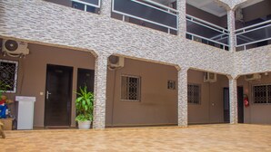 A courtyard with a tiled floor, a potted plant, and a building with multiple doors and windows. - Residences Hydlyss (Abidjan)