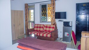A compact room with a sofa, a small TV, a refrigerator, and a door marked "CH-17". - Residences Hydlyss (Abidjan)