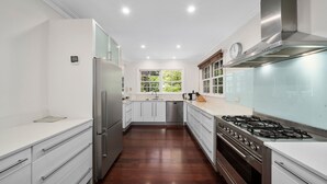 A modern kitchen with stainless steel appliances, white cabinetry, and a large window providing natural light. - Clanalpine Retreat  Leura (Leura)